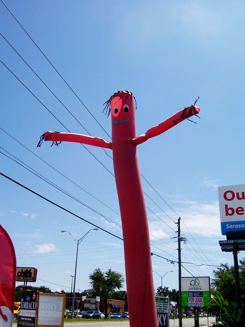 an outdoor sculpture with arms and legs standing next to a sign