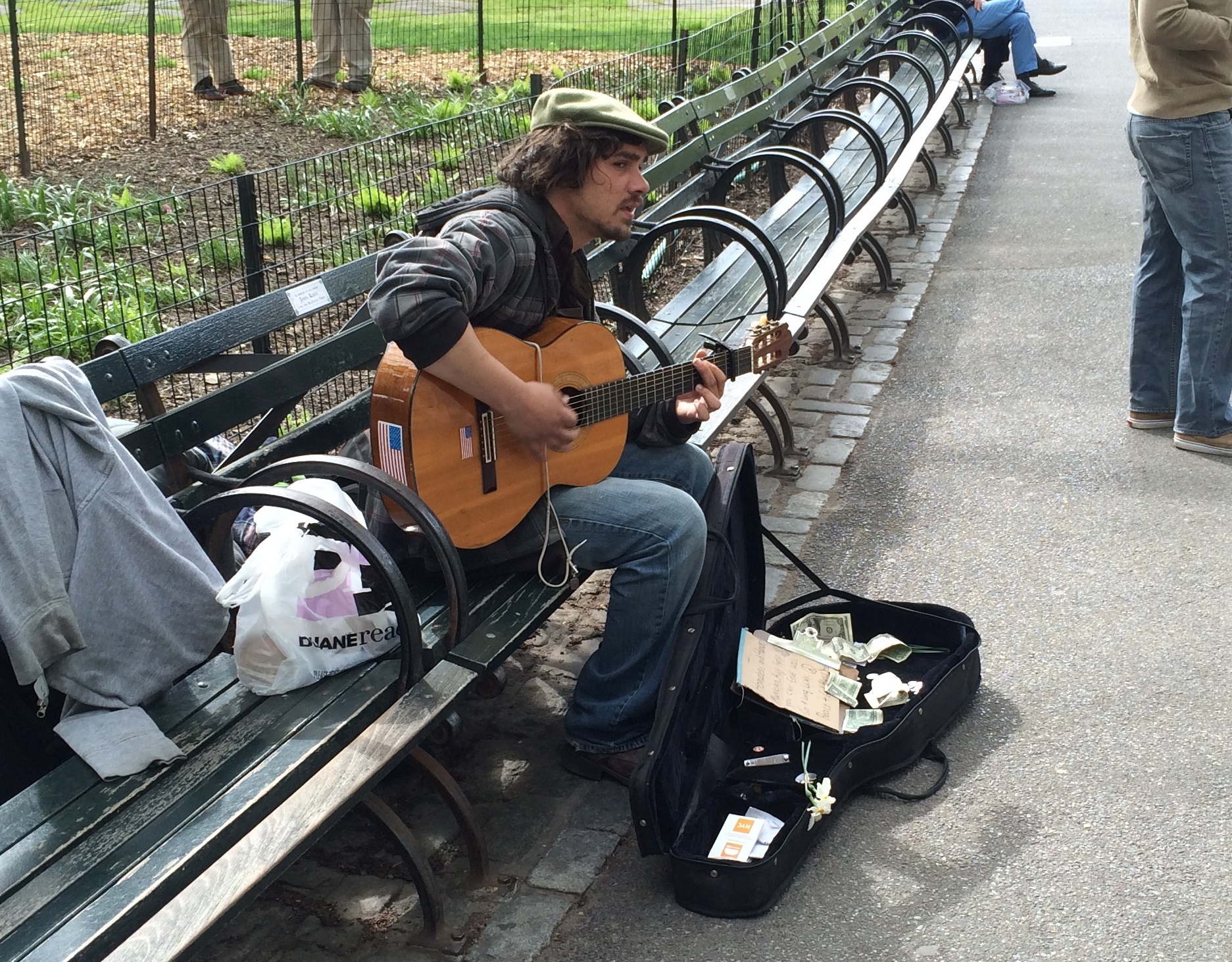 man playing guitar in park setting on bench