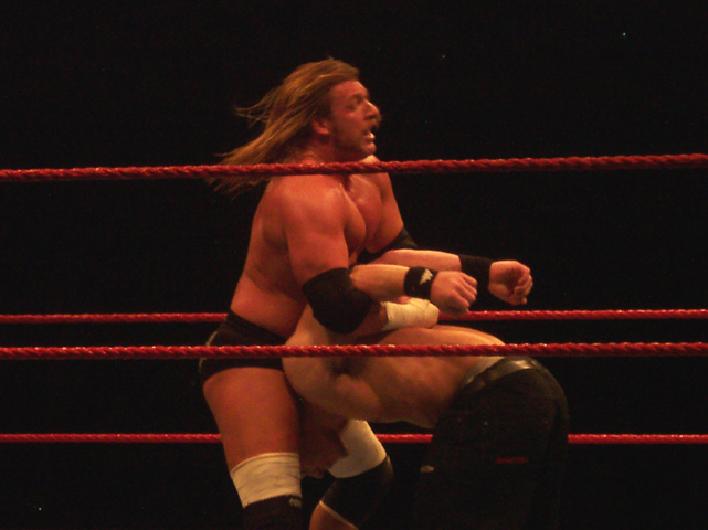 a shirtless wrestler holding up his knee as he stands in a rope ring