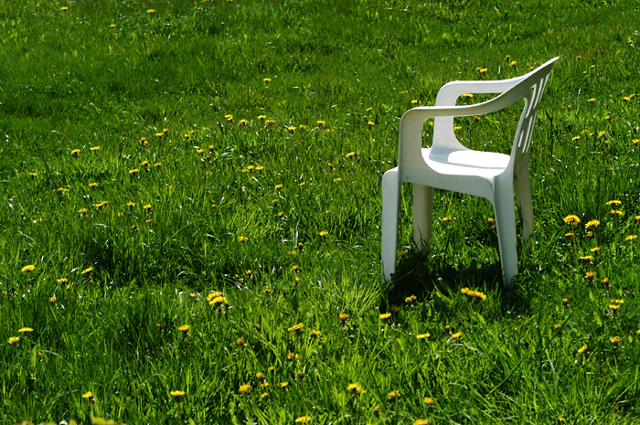 an empty plastic chair in the middle of a green field