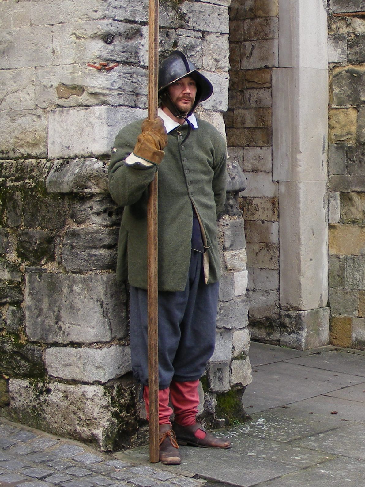 man in old costume posing next to brick wall