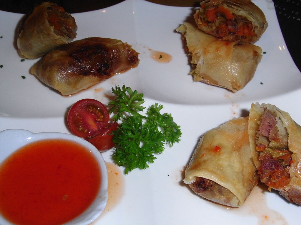 a white plate topped with rolled food next to a bowl of tomato soup