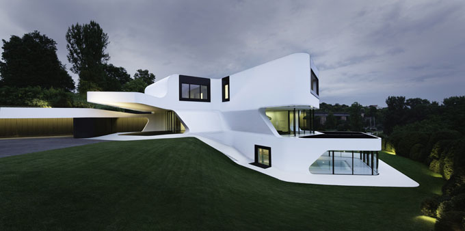 a curved white house surrounded by a grass covered hillside
