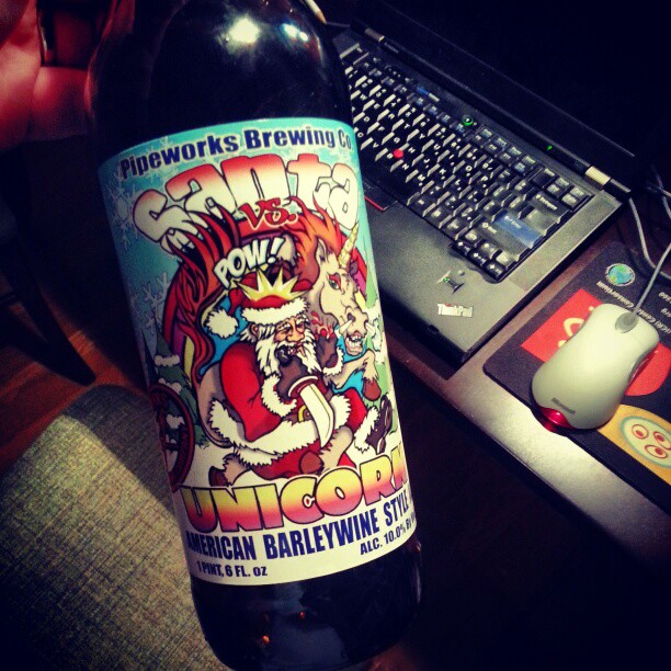 a bottle of beer with cartoony artwork on the label sits in front of a laptop computer