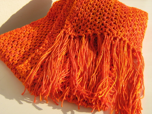 an orange knitted scarf is laying on a white surface