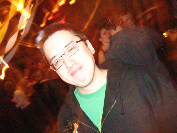 man in glasses with green shirt and black hoodie with lights in background