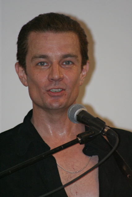 man speaking into microphone with black shirt and necklace