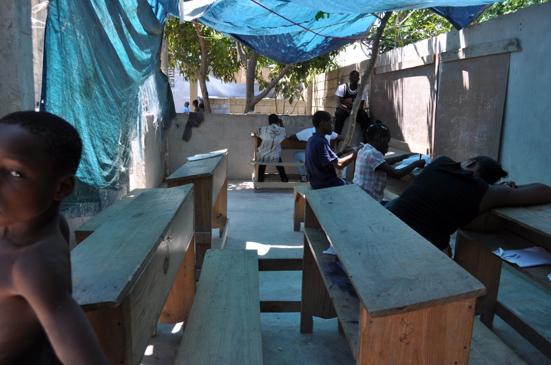 many children are in a makeshift classroom under an umbrella