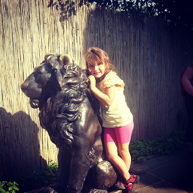 a little girl standing next to a bronze statue