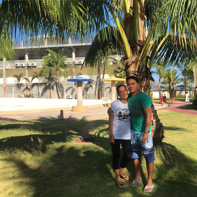 a man and woman posing near a palm tree