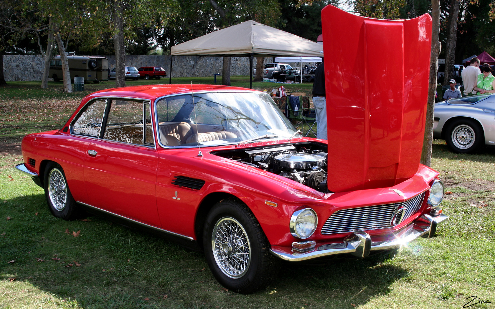 a vintage car with an open hood parked in the grass