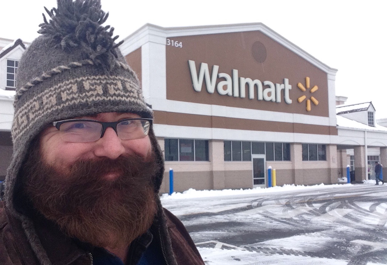 a man with glasses and a knit hat stands in front of a walmart building