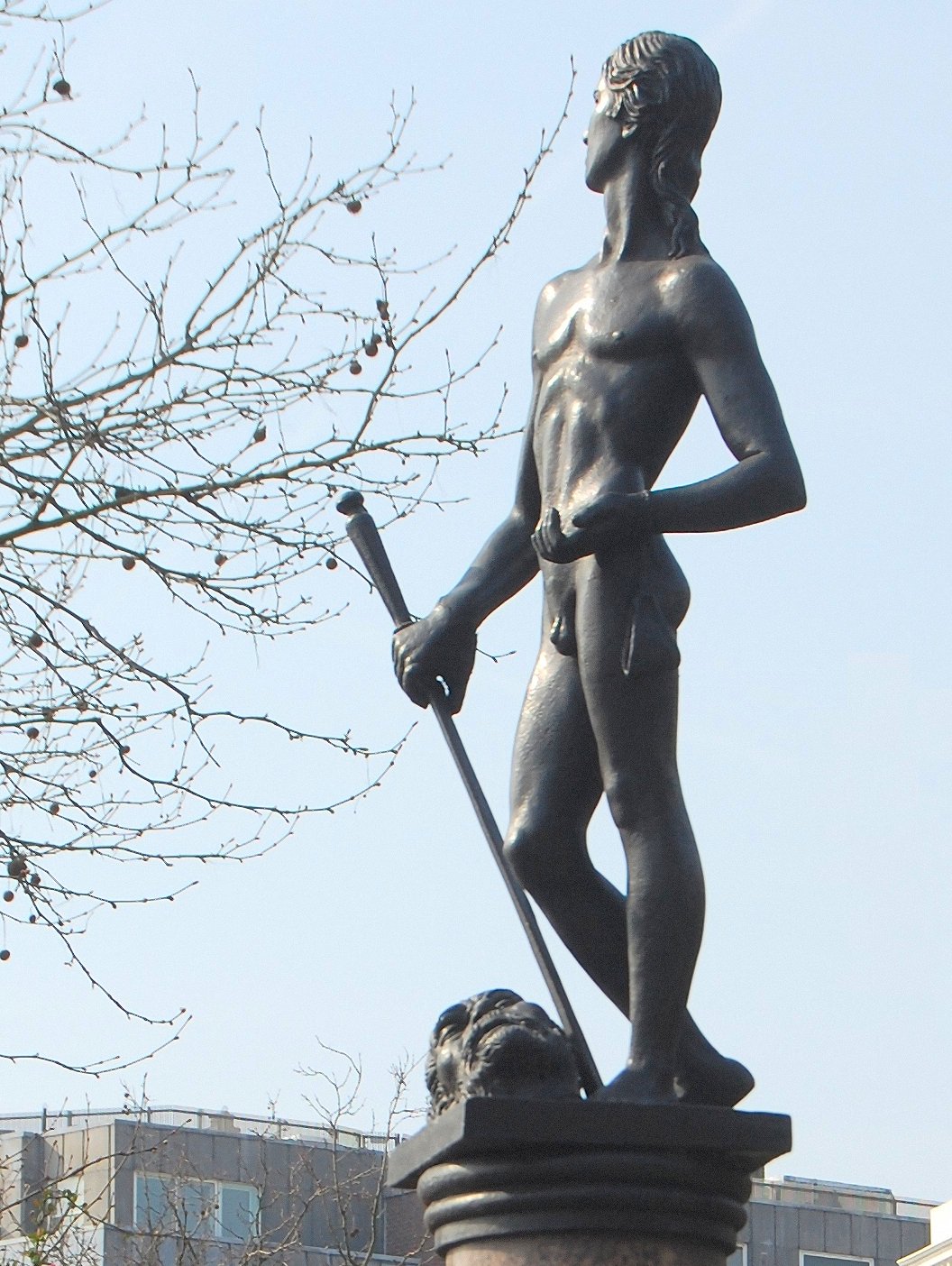 a statue in the shape of a male with a spear standing beside a building