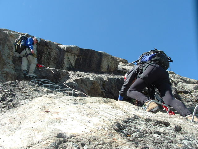 two people climbing up the side of a mountain