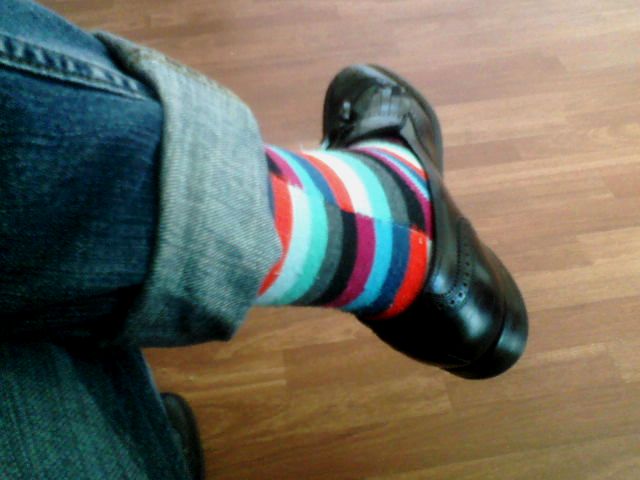 person in black loafers with a red, blue, green and pink striped sock