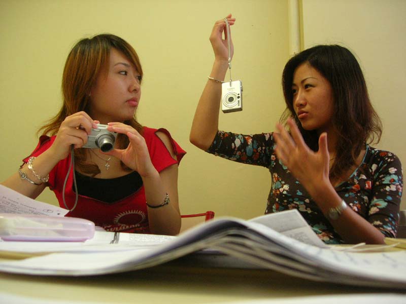 two woman sitting at a table with one of them holding a camera