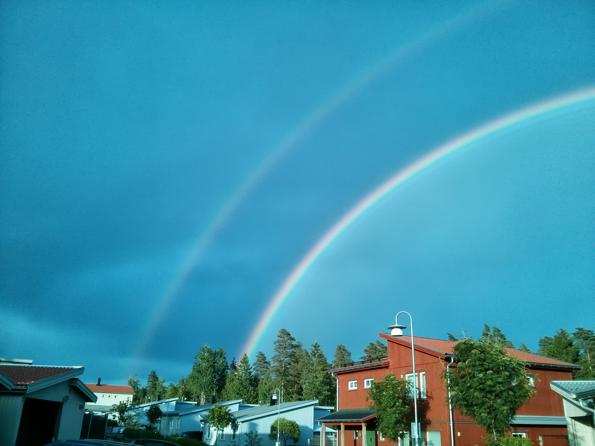 a double rainbow shining in the sky over a red house