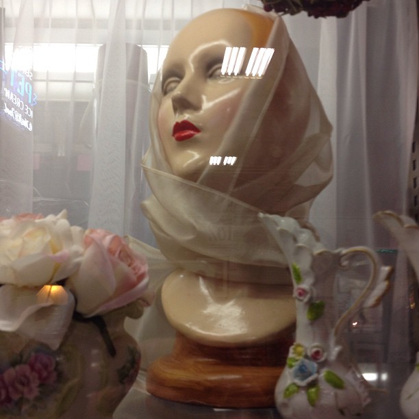 mannequin with a scarf over his head behind several vases