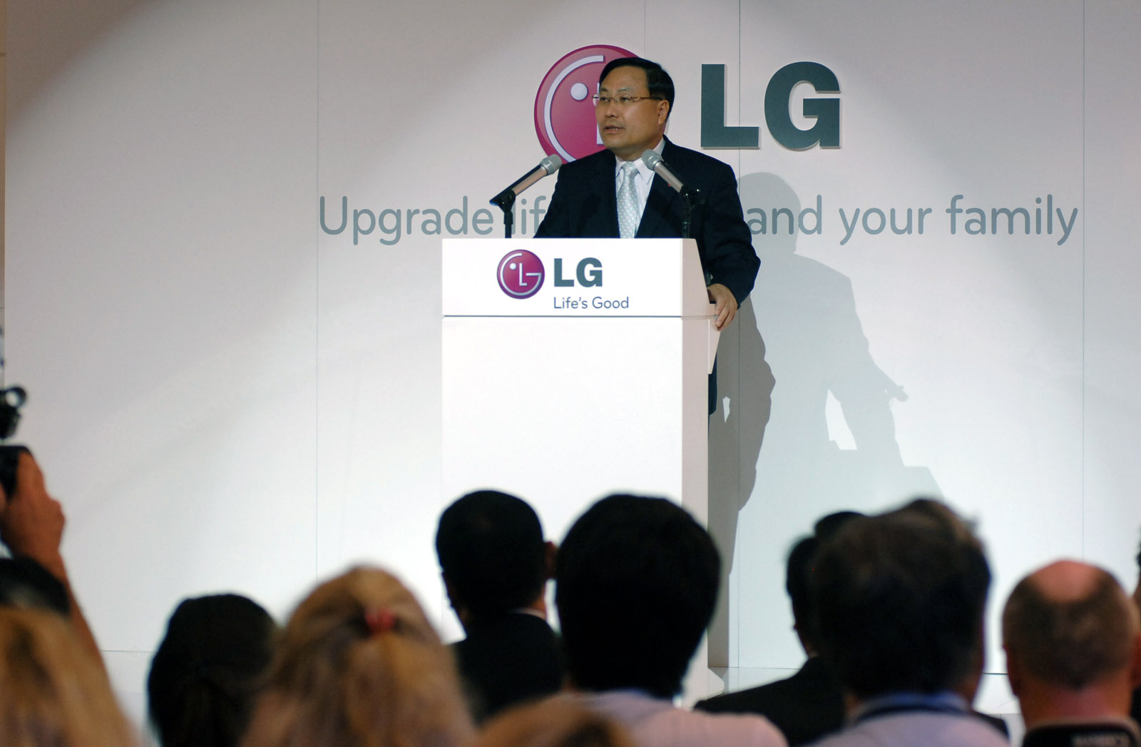 an asian man at a podium with his microphone extended, with the lg logo behind him