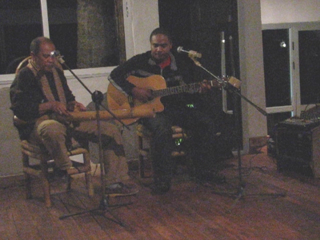 two men sitting in chairs singing into microphones while the rest is playing