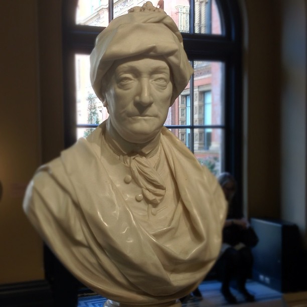 a statue in front of a window wearing a bonnet