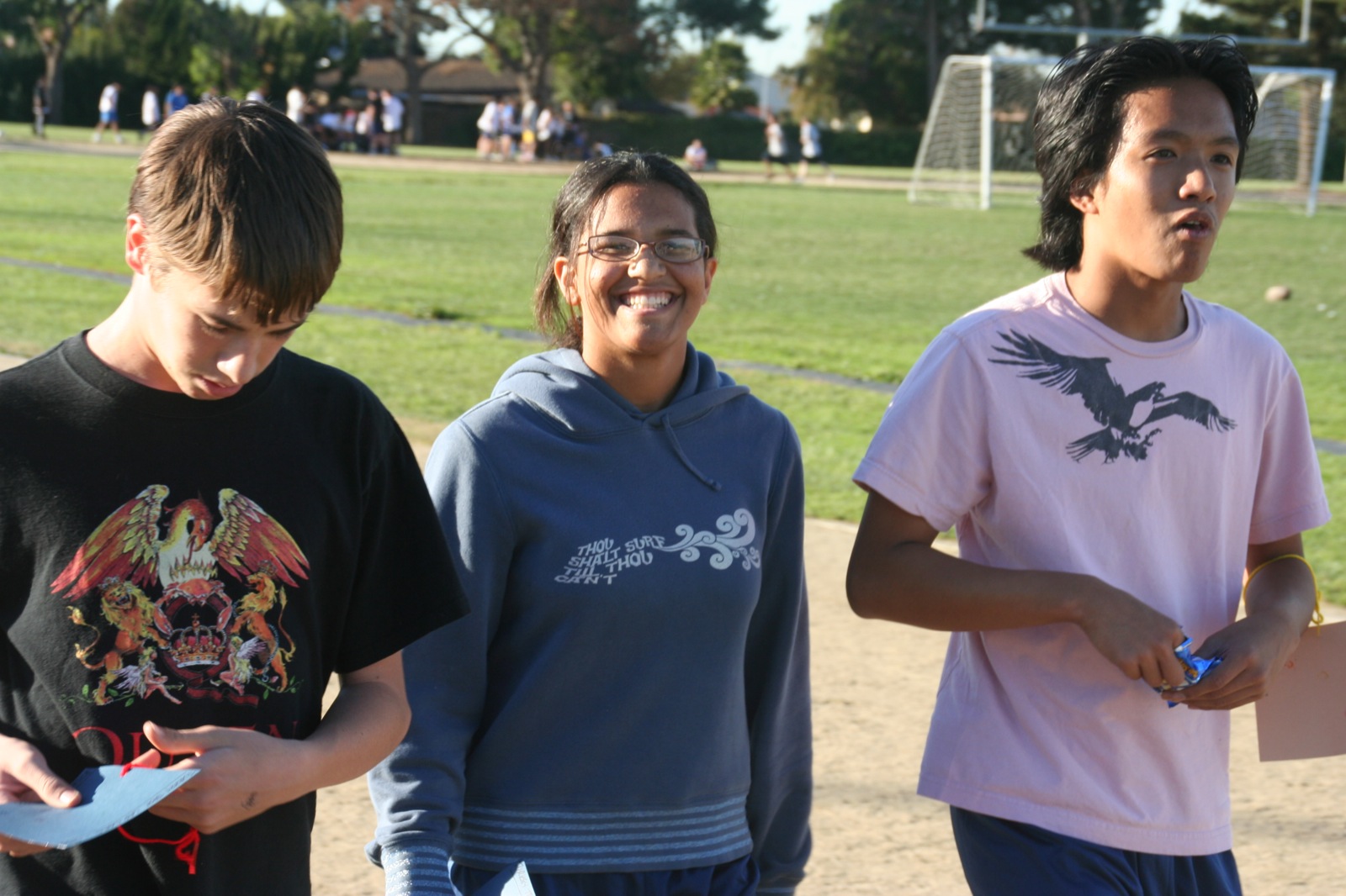 three boys looking over an electronic device while standing on a grass field