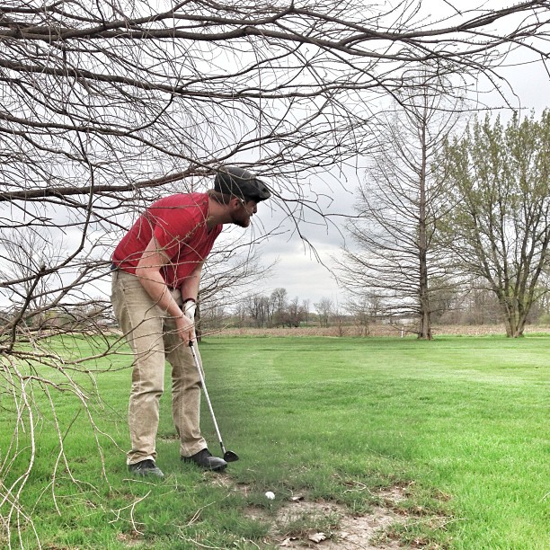 a man in a red shirt stands on the grass near a hole