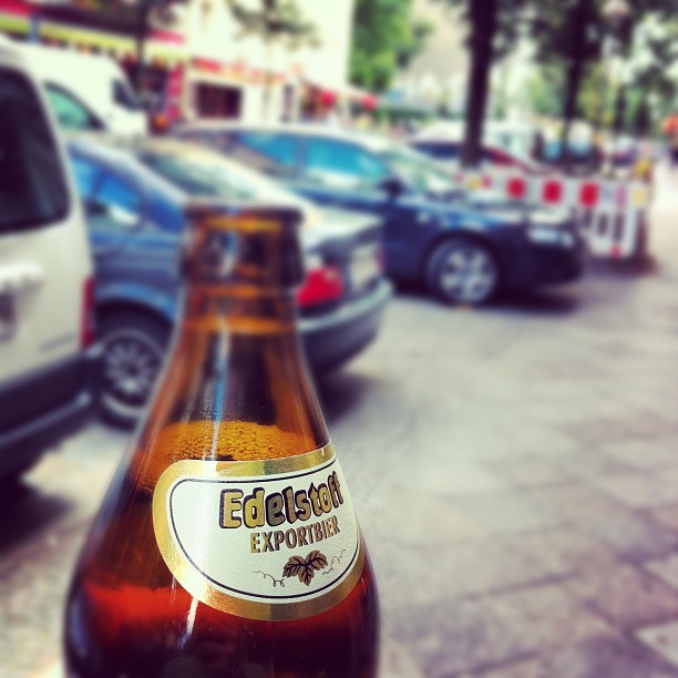 a close up view of a beer bottle on a sidewalk in front of parked cars