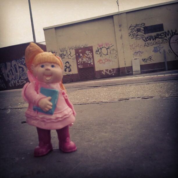 a toy figurine of a girl in pink is standing on a sidewalk