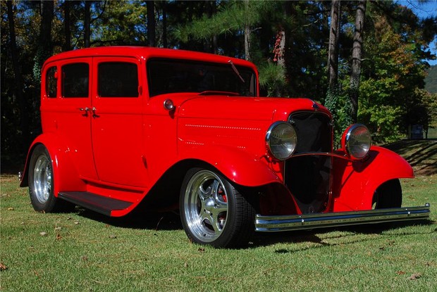 an antique style red car sitting in the grass