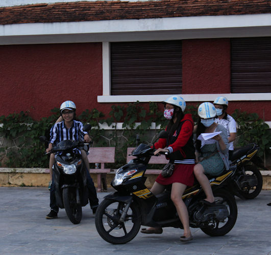 a woman riding a motorcycle with two other people wearing helmets