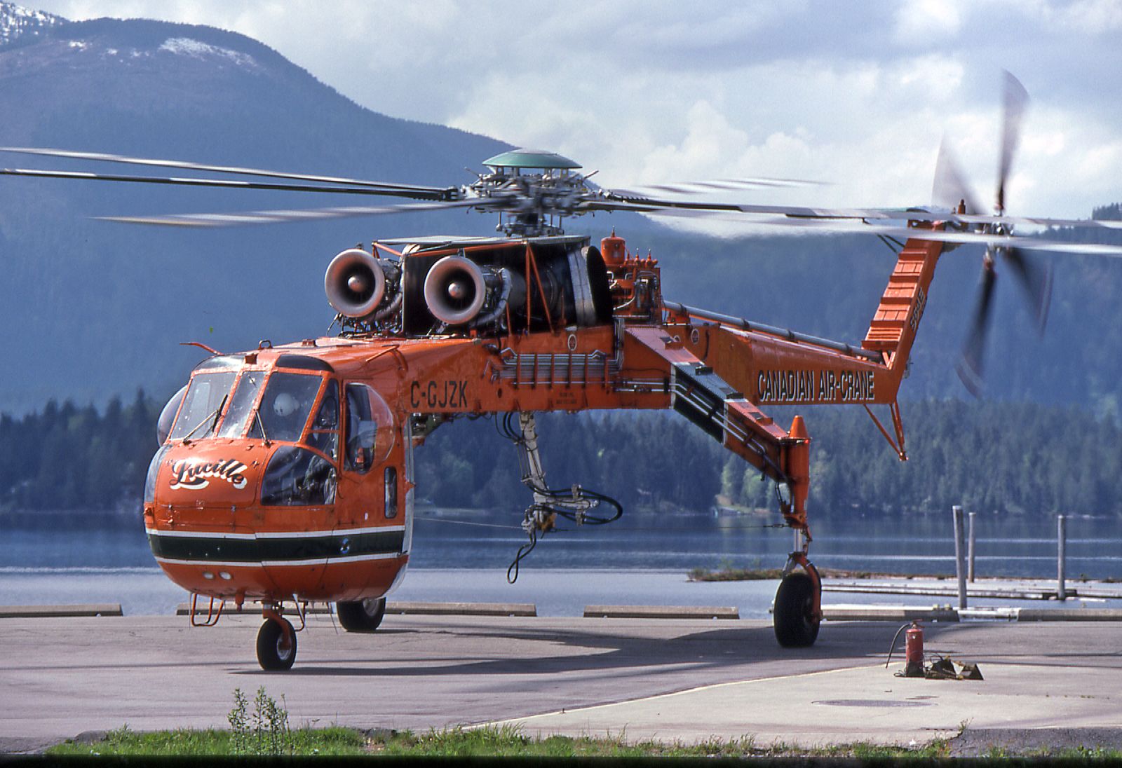 an orange helicopter on the ground with mountains in the background