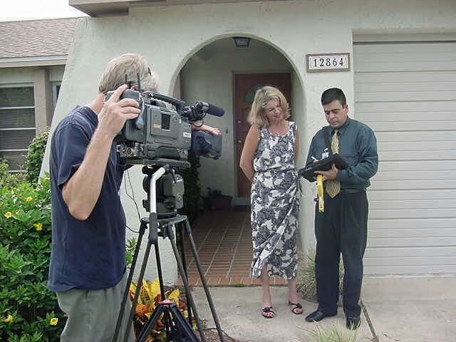 two men and a woman are outside of a house with a camera man