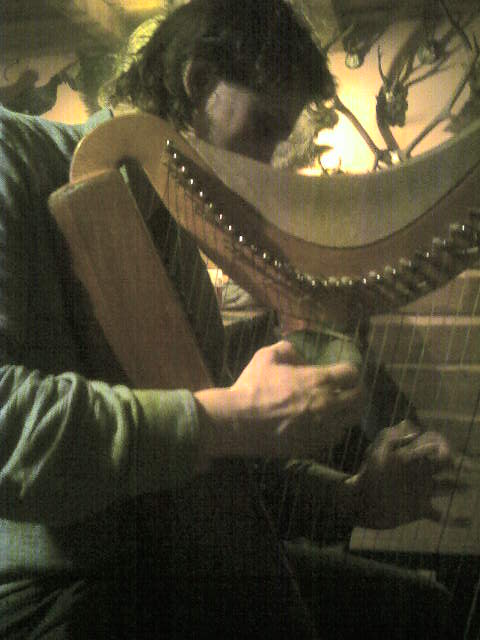 a man playing a large wooden harp while holding a cell phone