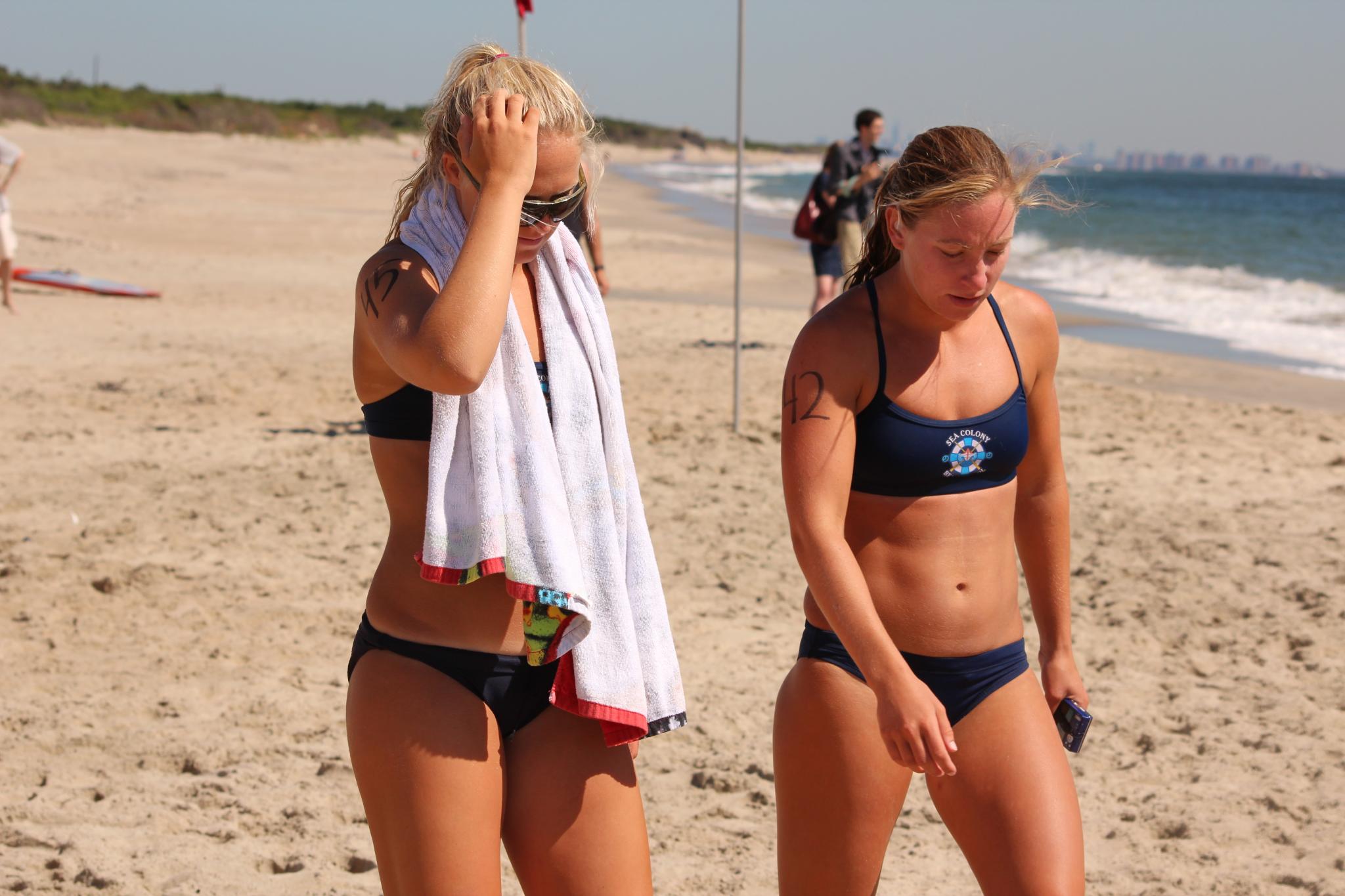 a couple of women standing on top of a beach next to a ocean