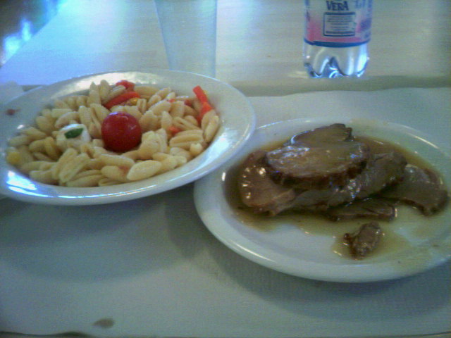 a plate with pasta, meat and vegetables on it and a plate with a tomato on it