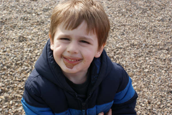 boy laughing in the park on gravel with rocks behind him