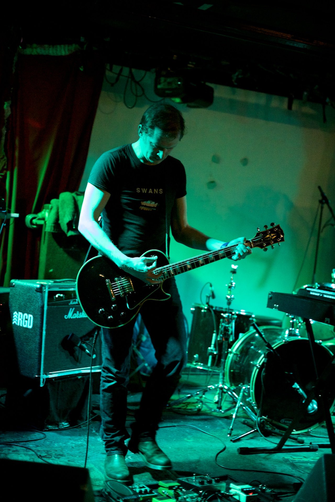 a man with guitar standing in front of a drum set