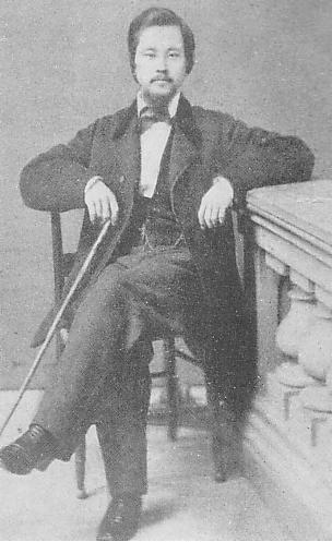a man wearing a bow tie and black jacket sitting on a chair
