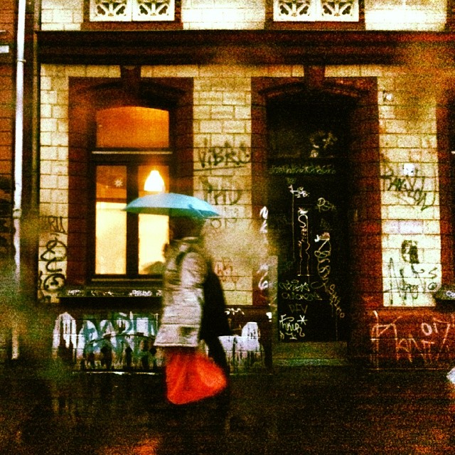a woman with an umbrella is walking past a brick building with writing on it