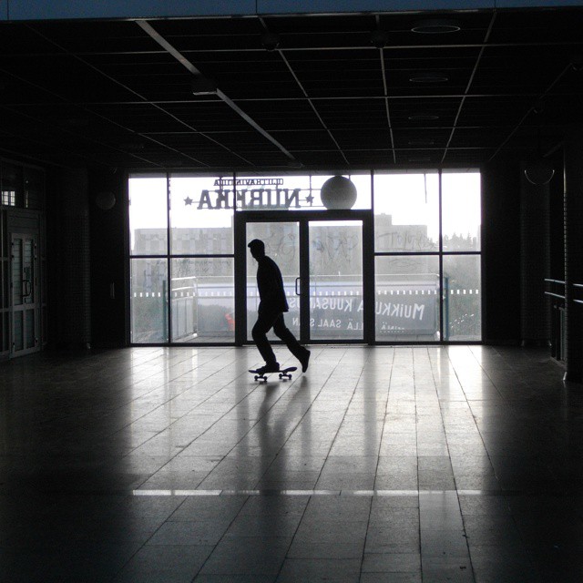 silhouetted man riding a skateboard on top of a tiled floor
