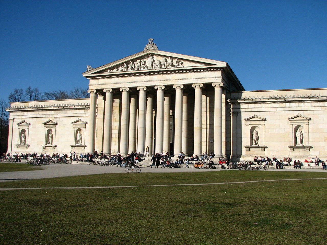 many people standing around a large building with many pillars