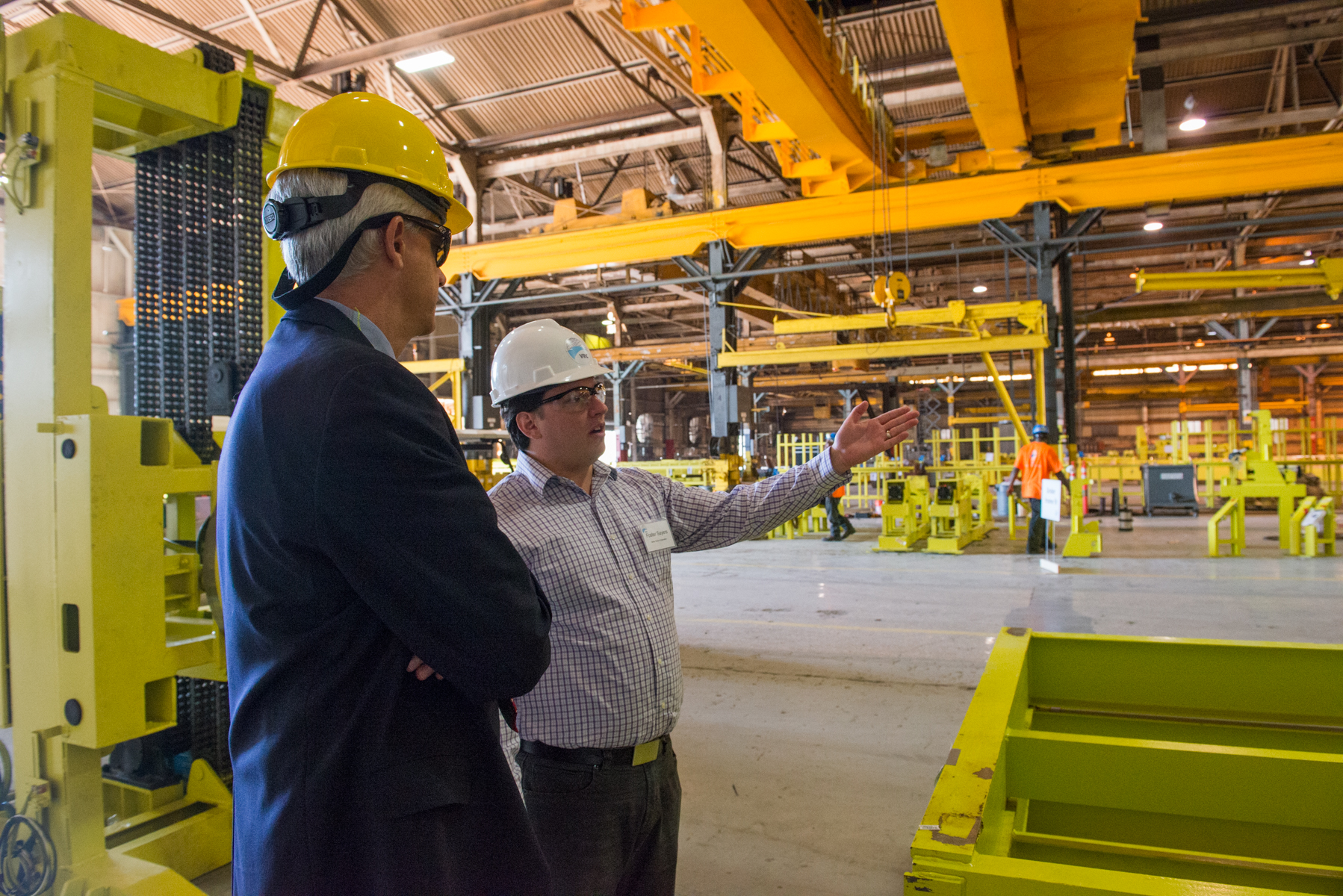 two men in hard hats stand next to an industrial machine