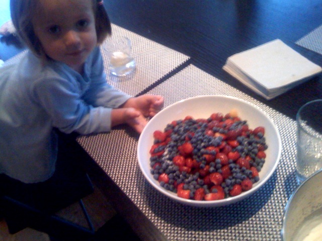 small child sitting at the table eating a berry salad
