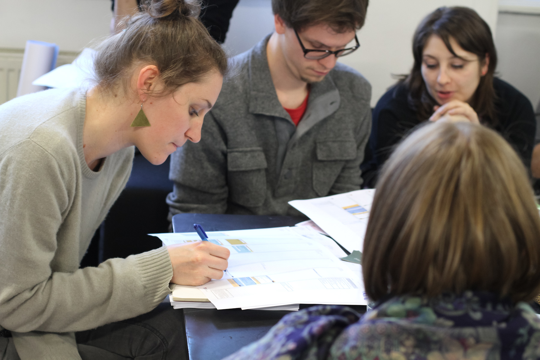 the girl is writing on some paper while others watch