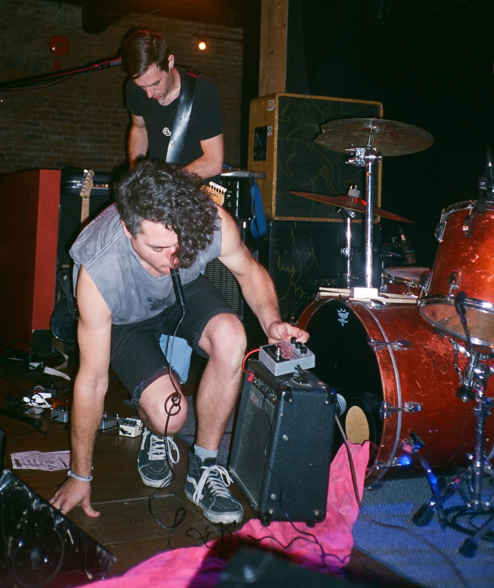 two men play drums in front of a red drum set