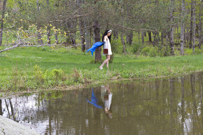 a woman is walking by a pond holding umbrellas