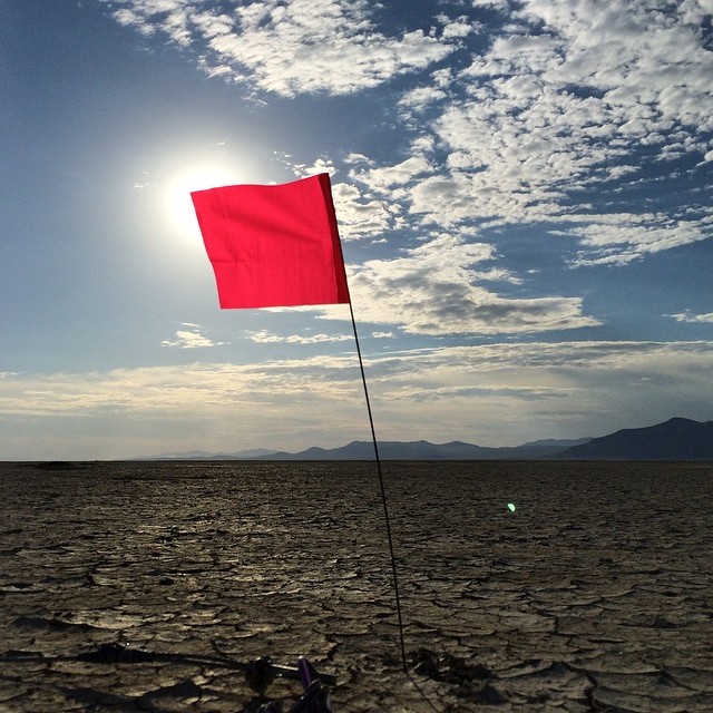 a lone red flag on the beach in front of the sun