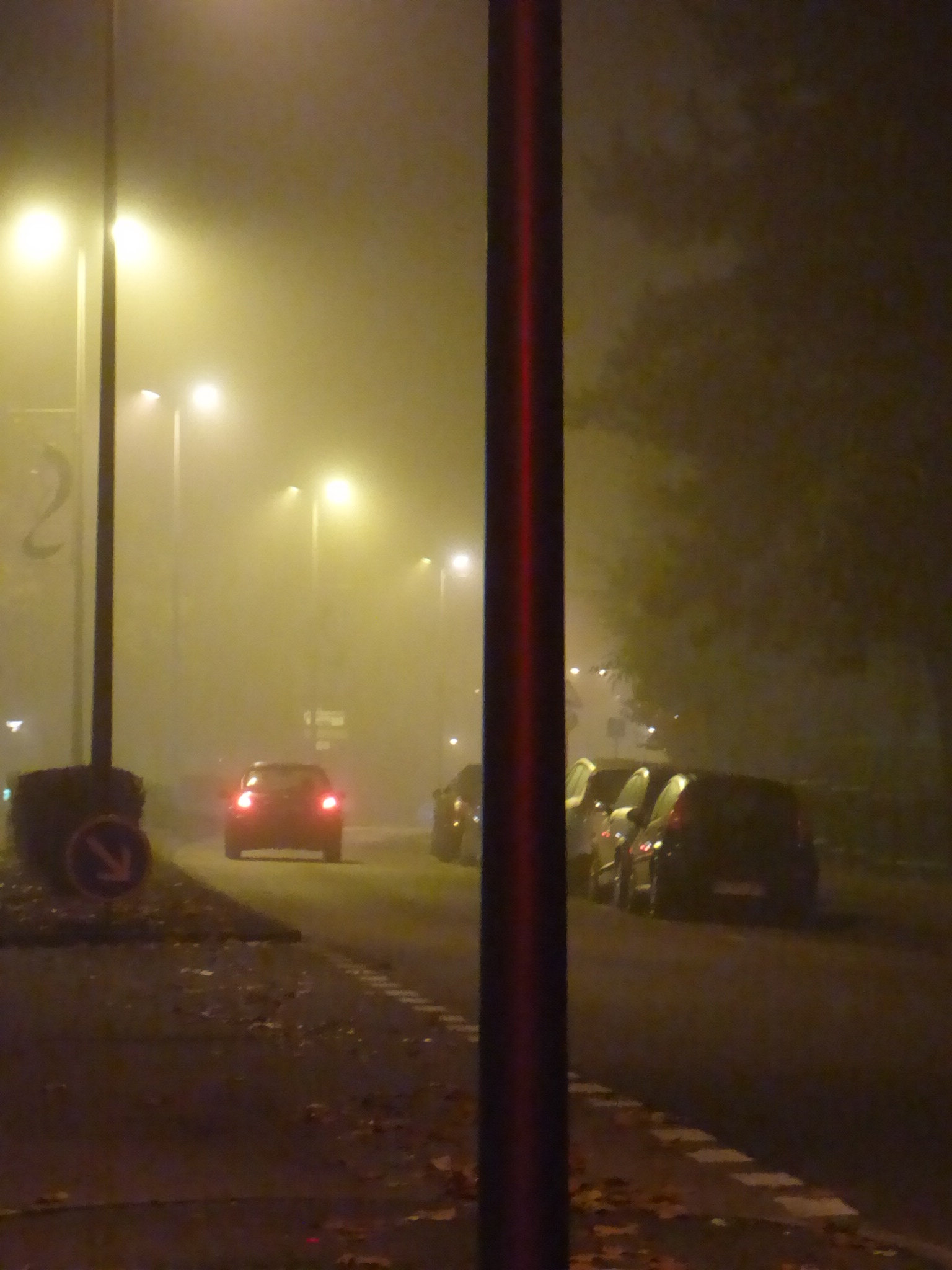 traffic at night in foggy street with parking lot near by