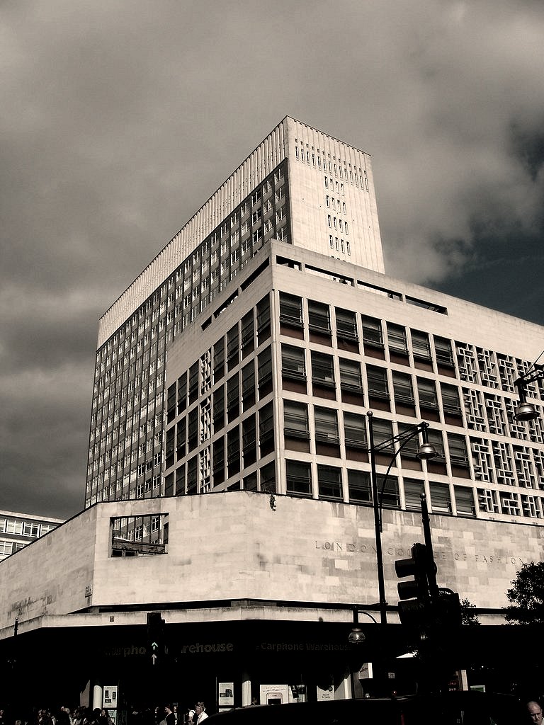 a tall building under a cloudy sky with people on the street